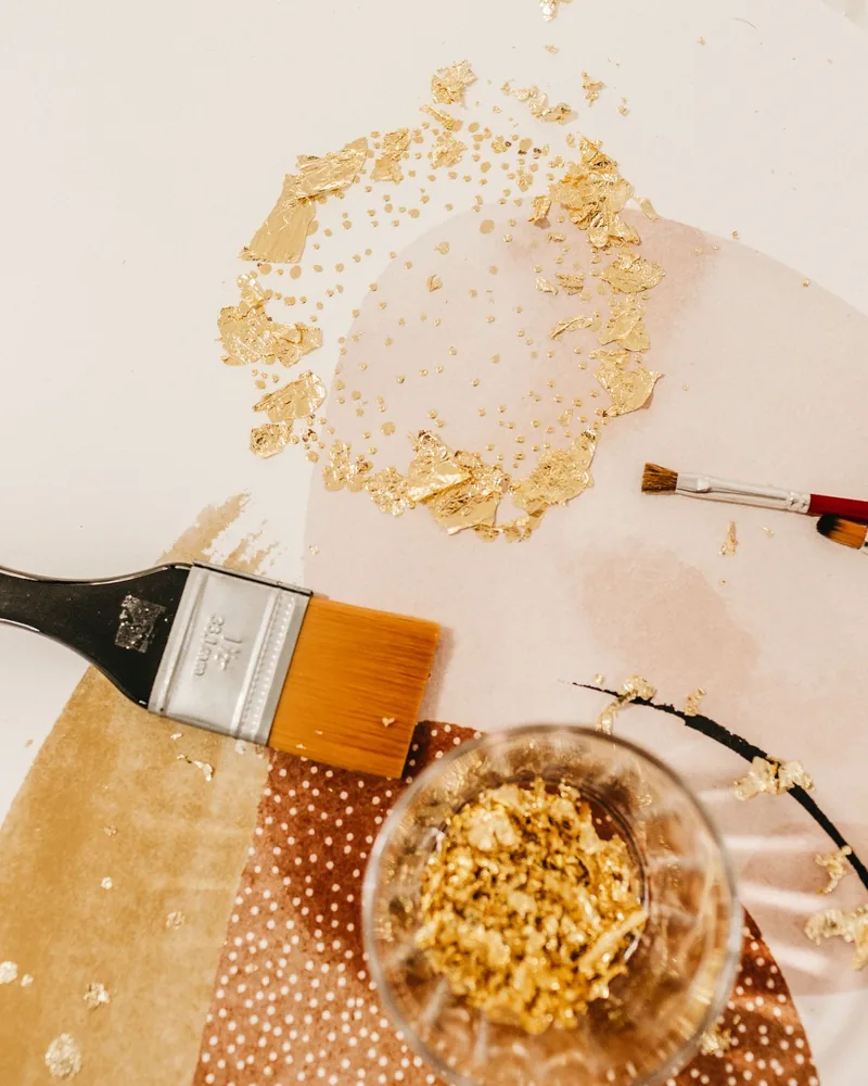 Pinceles de dorador y un recipiente de vidrio con polvo de oro sobre una mesa de trabajo