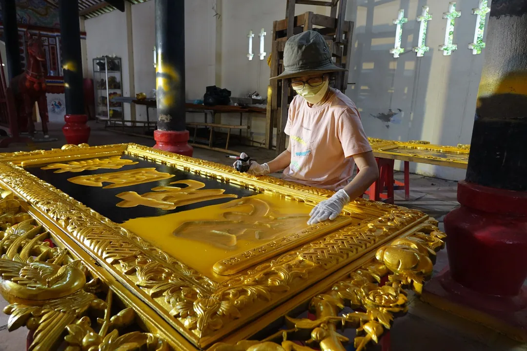 Manos de un dorador aplicando pan de oro sobre la talla de un panel decorativo